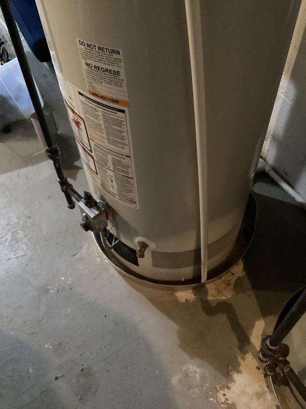 Responded to residential water heater leak. Upon arrival, inspected tanked water heater unit and identified active leak at base with visible water accumulation on concrete floor and corrosion staining around lower fittings. Assessed brass drain valve and bottom connections showing signs of deterioration and moisture intrusion. Drip pan exhibited rust discoloration indicating prolonged exposure to leaking water. Documented condition with photographs showing extent of water damage and compromised seals at tank base. Recommended replacement of unit due to tank integrity failure and advised customer of leak source and necessary corrective action.