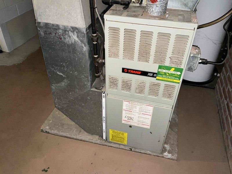 Conducted comprehensive assessment of existing HVAC system for replacement estimate. Evaluated indoor Trane XE 8 furnace unit located in basement utility area and outdoor air conditioning condenser units showing significant weathering and age-related deterioration. Documented current equipment condition, including visible rust, debris accumulation, and protective covering on outdoor units. Photographed existing installation configuration, ductwork connections, and equipment placement to provide accurate replacement options and specifications for complete system upgrade.
