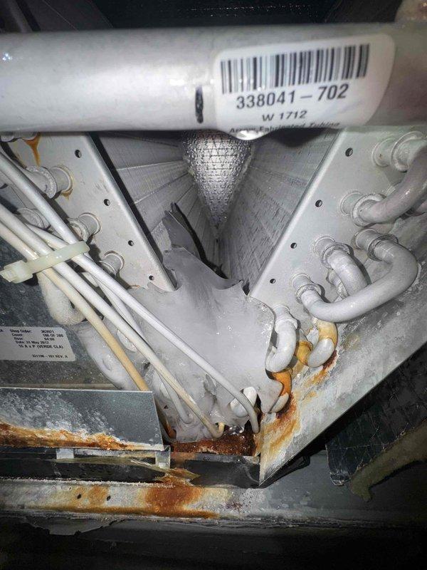 Responded to no cooling complaint on central air conditioning system with upstairs temperature unable to maintain setpoint. Upon inspection, discovered significant rust and corrosion on evaporator coil assembly, metal framework, and drain pan, indicating long-term moisture exposure and potential refrigerant leaks. Documented extensive deterioration of internal components including compromised structural integrity of unit housing and active corrosion on critical refrigerant line connections, which would prevent proper system operation and cooling capacity.
