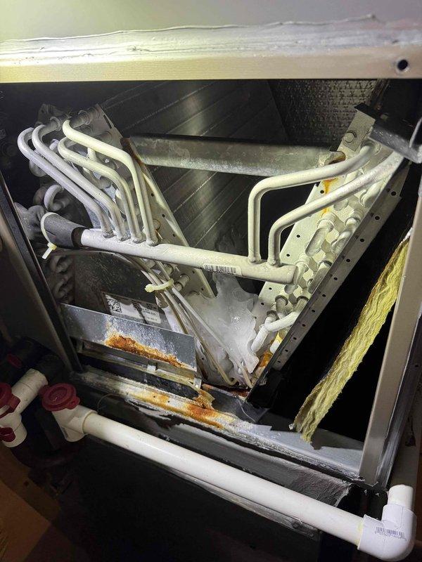 Responded to no cooling complaint on central air conditioning system with upstairs temperature unable to maintain setpoint. Upon inspection, discovered significant rust and corrosion on evaporator coil assembly, metal framework, and drain pan, indicating long-term moisture exposure and potential refrigerant leaks. Documented extensive deterioration of internal components including compromised structural integrity of unit housing and active corrosion on critical refrigerant line connections, which would prevent proper system operation and cooling capacity.