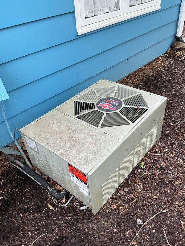 Responded to no cooling complaint with thermostat communication issue. Upon arrival, found outdoor condensing unit installed on mulch bed against building exterior with visible weathering and damaged electrical connection box showing signs of deterioration at conduit entry point. Inspected system components, documented equipment condition including refrigerant line connections and manufacturer specifications, and assessed thermostat communication failure preventing compressor operation.