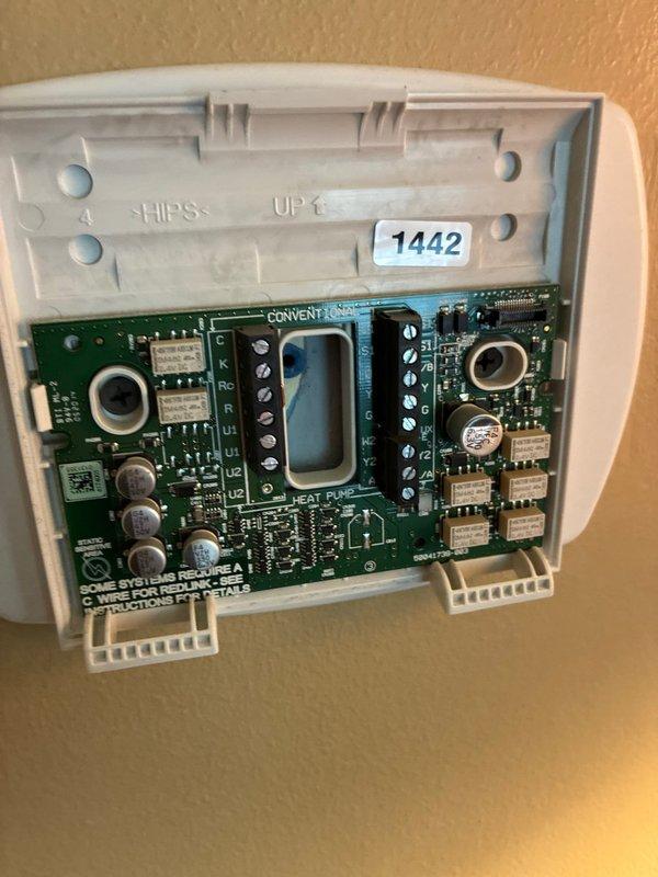 Conducted on-site evaluation of existing HVAC system for equipment replacement options. Inspected thermostat control system, documenting internal wiring configuration and terminal connections on the conventional/heat pump compatible circuit board. Assessed outdoor condensing unit located on rear patio, noting current equipment condition and photographed installation site for replacement planning purposes.