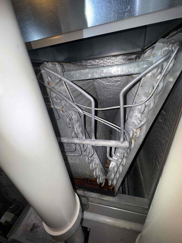 # HVAC Cooling Maintenance Completed

Performed comprehensive cooling system maintenance on residential HVAC unit. Upon inspection, discovered evaporator coil completely covered in thick frost and ice buildup, indicating restricted airflow or refrigerant system abnormality. Identified significant corrosion and rust on pipe mounting brackets and hardware at condensate drain assembly, with visible water damage and staining on surrounding floor surfaces suggesting chronic moisture issues or previous drain line failures. Documented system conditions including compromised drainage components and frozen evaporator coil requiring immediate attention to prevent compressor damage and restore proper cooling operation.