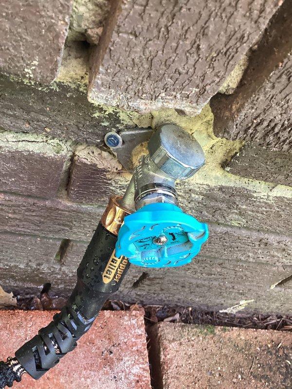 Responded to service call for two faucet issues: a leaking outdoor hose bib and difficulty adjusting water temperature on a kitchen faucet. Inspected the exterior spigot with blue handle mounted on stucco wall and identified source of leak at valve assembly. Examined the modern pull-down kitchen faucet with brushed finish and spray head to diagnose temperature control problem with the single-handle cartridge system.