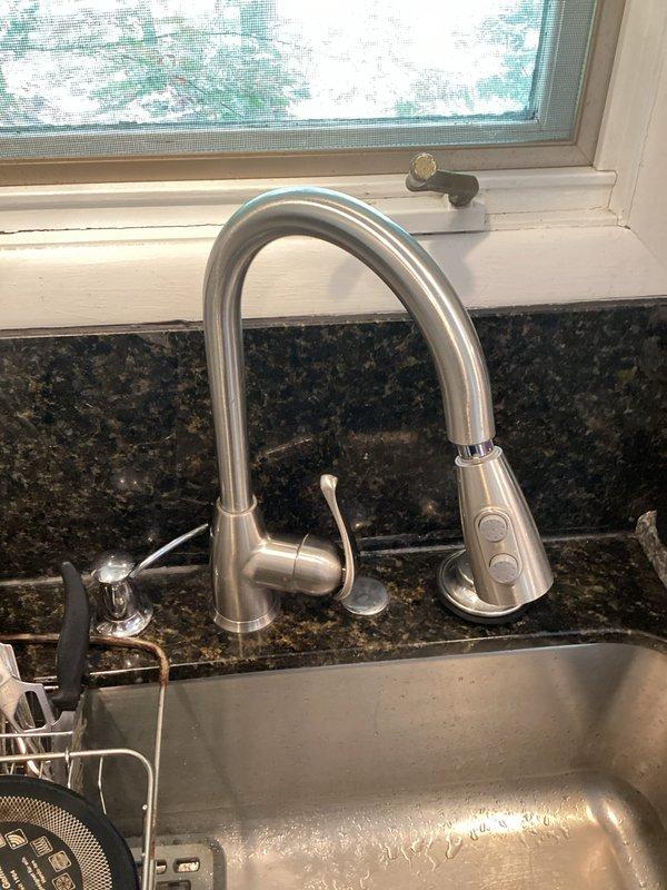 Responded to service call for two faucet issues: a leaking outdoor hose bib and difficulty adjusting water temperature on a kitchen faucet. Inspected the exterior spigot with blue handle mounted on stucco wall and identified source of leak at valve assembly. Examined the modern pull-down kitchen faucet with brushed finish and spray head to diagnose temperature control problem with the single-handle cartridge system.