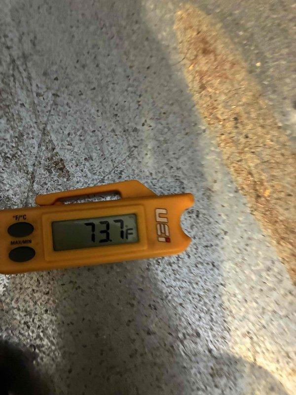 Returned to unit after previous dye injection to conduct leak search on HVAC system. Performed thorough inspection of compressor and refrigerant lines using UV light detection method. Documented current system conditions including temperature readings of 73.1°F and visual evidence of component deterioration. Identified heavily corroded compressor housing with significant rust accumulation and oxidation present on copper refrigerant lines. Captured photographic documentation of leak search findings and overall equipment condition for service records.