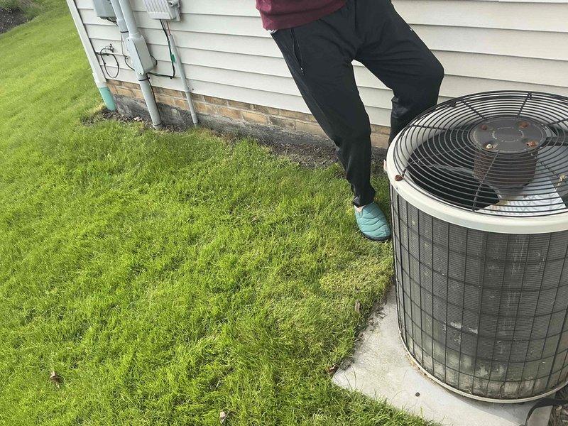 Conducted on-site evaluation of existing HVAC system for replacement estimate. Inspected outdoor condenser unit positioned on concrete pad adjacent to residential structure with white siding, assessing equipment condition and installation accessibility. Documented indoor mechanical components including ductwork configuration, PVC condensate drainage system with U-trap assembly, and associated plumbing connections in utility space. Photographed existing system layout to provide comprehensive replacement options for customer consideration.