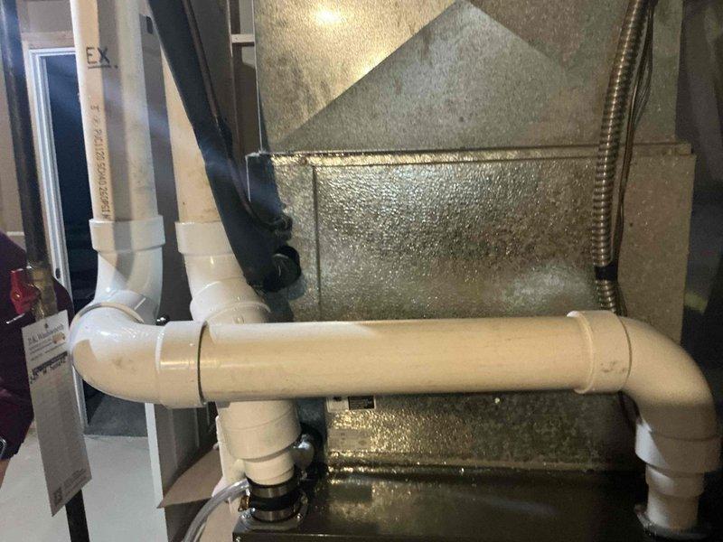 Conducted on-site evaluation of existing HVAC system for replacement estimate. Inspected outdoor condenser unit positioned on concrete pad adjacent to residential structure with white siding, assessing equipment condition and installation accessibility. Documented indoor mechanical components including ductwork configuration, PVC condensate drainage system with U-trap assembly, and associated plumbing connections in utility space. Photographed existing system layout to provide comprehensive replacement options for customer consideration.