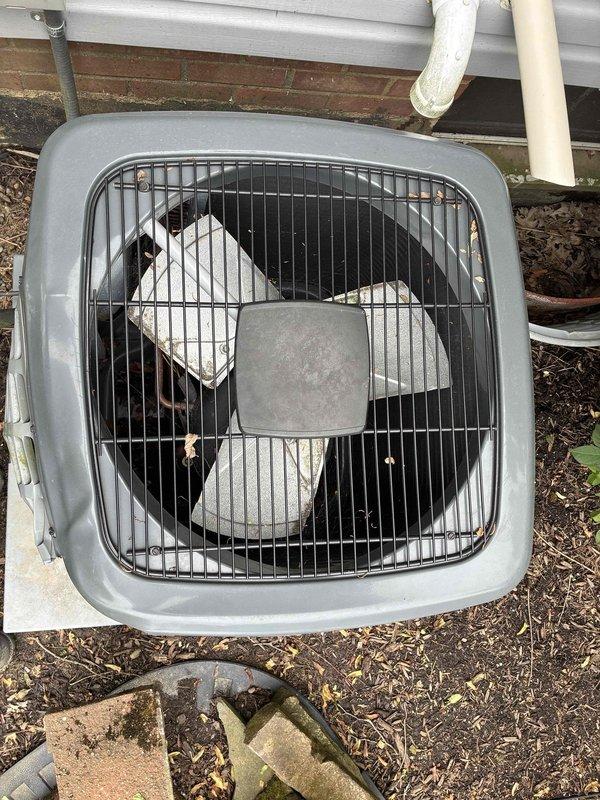 Responded to service call for air conditioning unit damaged by ice accumulation. Upon arrival, inspected outdoor condenser unit and found weathered housing with accumulated dirt and debris on louvered grilles and fan assembly. Assessed refrigerant lines, electrical connections, and overall system condition following ice-related damage. Documented equipment condition with photographs showing three-blade fan assembly, protective wire grille, and exterior components. Unit operational after inspection, with customer advised of findings.