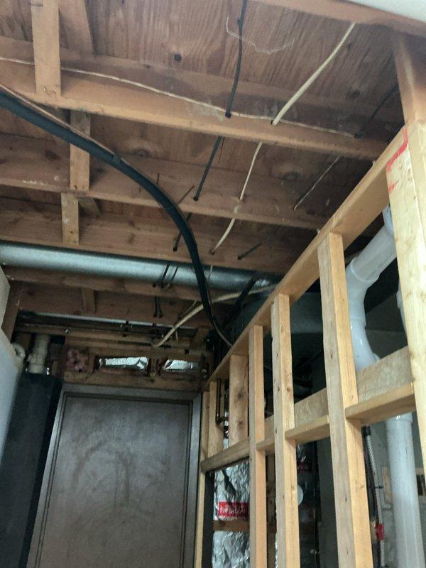 Completed comprehensive whole-home electrical inspection, evaluating all visible wiring, panels, circuits, and electrical components throughout the property. Inspected unfinished basement area with exposed ceiling joists, documenting multiple cable runs including black flexible conduits and various gauge wiring secured to structural members. Examined exterior electrical service entrance, meter installation, and associated conduit routing on home's exterior wall. Investigated reported doorbell wiring issue allegedly damaged during previous year's installation, tracing circuits and connections to identify any severed or compromised conductors. Documented findings with photographs of electrical infrastructure, including basement utility area framing and exterior service equipment for record-keeping and future reference.