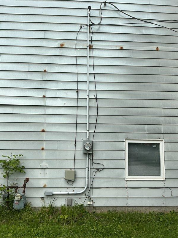 Completed comprehensive whole-home electrical inspection, evaluating all visible wiring, panels, circuits, and electrical components throughout the property. Inspected unfinished basement area with exposed ceiling joists, documenting multiple cable runs including black flexible conduits and various gauge wiring secured to structural members. Examined exterior electrical service entrance, meter installation, and associated conduit routing on home's exterior wall. Investigated reported doorbell wiring issue allegedly damaged during previous year's installation, tracing circuits and connections to identify any severed or compromised conductors. Documented findings with photographs of electrical infrastructure, including basement utility area framing and exterior service equipment for record-keeping and future reference.