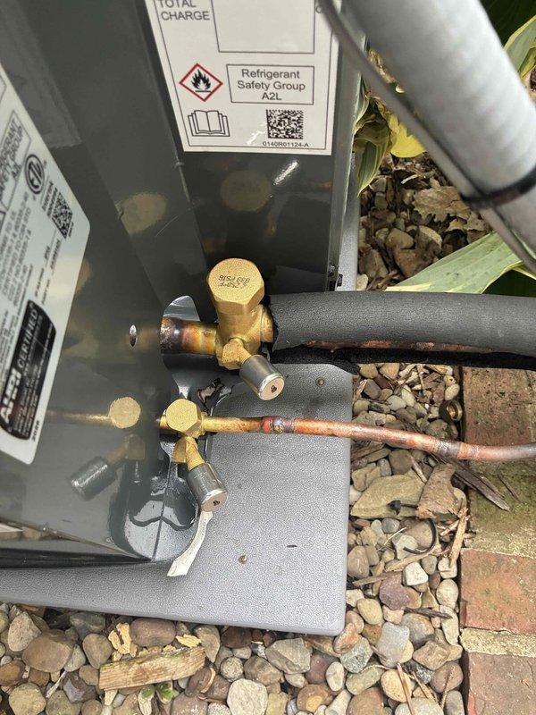 Completed installation of new residential air conditioning system. Mounted outdoor condensing unit on gravel pad adjacent to home exterior, installed electrical disconnect box with proper conduit connections, and routed refrigerant lines with brass service valves and appropriate insulation. Installed white PVC condensate drain line with proper pitch and termination, verified refrigerant charge levels per manufacturer specifications, and ensured all electrical and mechanical connections meet code requirements for safe operation.