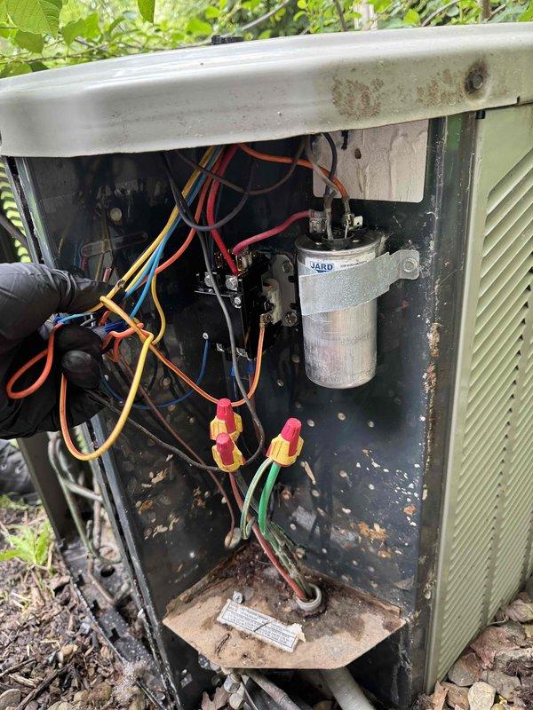 Responded to emergency no-cooling call on 10-15 year old central air conditioning system. Upon arrival, confirmed outdoor condenser fan motor was operational but unit was not producing cool air. Removed access panel to inspect electrical components and found capacitor with visible signs of failure. Interior of condenser unit showed significant accumulation of debris, dirt, and organic matter around capacitor and internal components, indicating extended period without maintenance. 

Tested capacitor with multimeter and confirmed readings were outside manufacturer specifications, preventing compressor from starting. Disconnected power and safely discharged failed capacitor. Removed defective unit and installed new replacement capacitor with proper microfarad rating for system. Reconnected all electrical connections using wire nuts and verified secure terminations on all colored wire leads.

Cleaned debris accumulation from interior compartment to prevent future airflow restriction and co