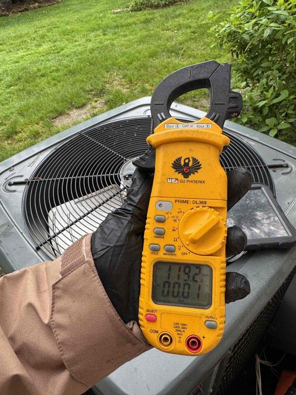 Performed routine cooling system maintenance on residential outdoor condensing unit. Conducted operational testing and electrical measurements using digital clamp meter to verify proper amperage draw and system performance. Unit operating within normal parameters with fan motor functioning correctly and adequate airflow through condenser coils.