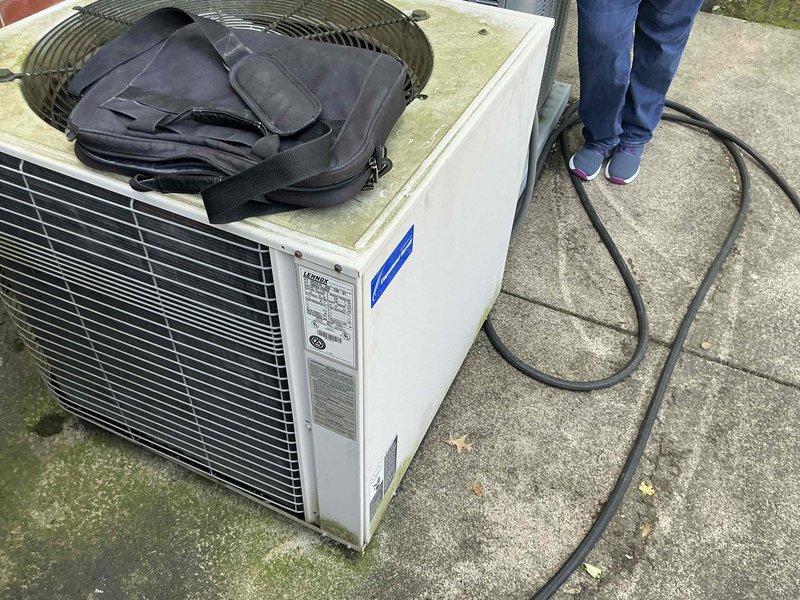 Conducted on-site assessment of existing outdoor air conditioning condenser unit to provide replacement options. Documented current equipment condition, noting weathered housing, aged components, and system specifications visible on manufacturer label. Captured detailed photographs of unit placement, surrounding concrete pad with visible deterioration, and proximity to building structure for accurate replacement planning and equipment sizing recommendations.