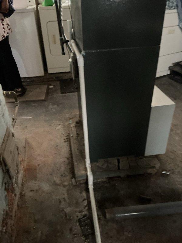 Responded to service call for AC system leak in basement area. Upon inspection, identified significant water discharge from condensate drain line where piping transitions from interior to exterior wall. Condensate line was experiencing improper drainage, causing water to leak onto basement floor as evidenced by moisture staining and discoloration on concrete surface. Traced piping from air handler unit through wall penetration to exterior condensate pump junction box. Cleared obstruction from drain line, verified proper pitch and flow, and tested system operation. Condensate now draining properly through exterior Diversitech pump assembly with no interior leakage detected.