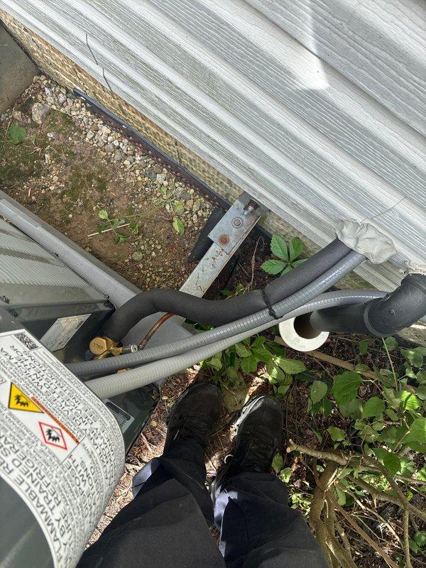 Completed full air conditioning system installation at residential property. Installed new outdoor condensing unit on ground-level pad with proper clearances from structure. Routed and connected refrigerant line set with insulation and protective conduit, secured all brass fittings and connections. Unit positioned adjacent to corrugated metal siding with adequate airflow access. Verified proper placement among existing landscaping to maintain equipment ventilation while providing natural screening. System installed, connections tightened, and unit left operational.