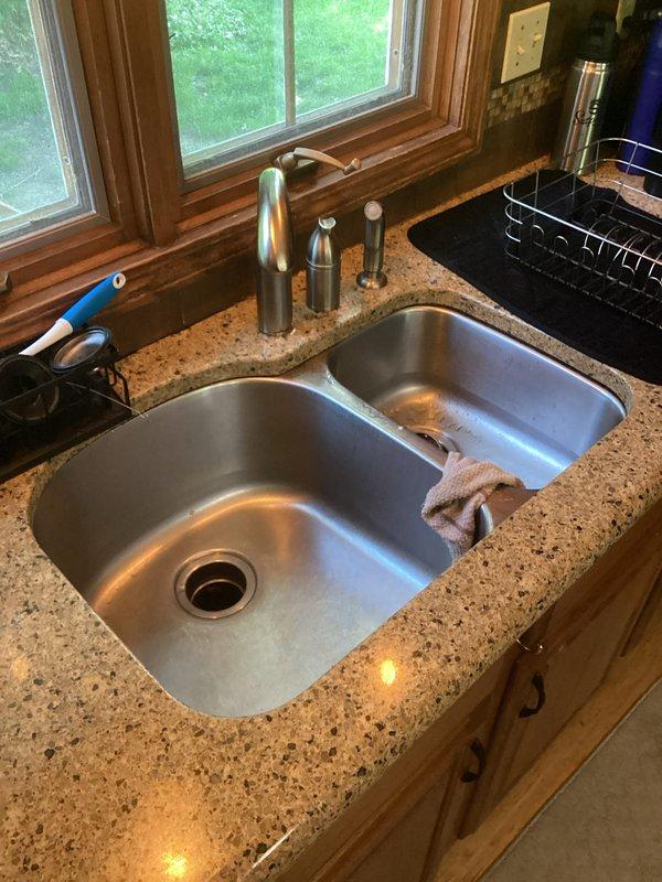 Provided estimate for installation of customer-supplied kitchen faucet in double-basin sink configuration. Assessed existing plumbing setup including undermount stainless steel sink with granite countertop, current faucet with soap dispenser and spray nozzle, and under-sink components including garbage disposal unit and PVC drainage system. Evaluated workspace access and confirmed compatibility for new faucet installation.