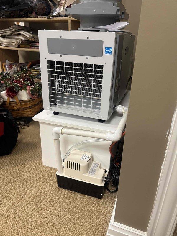 Completed installation of dehumidifier system with condensate pump and drainage assembly for portable air conditioning unit. Installed 3/4" PVC piping and condensate tubing to properly route moisture removal from the dehumidifier through the condensate pump. Configured two-tier shelving system to accommodate both the air conditioning unit and condensate management equipment, ensuring proper drainage flow and operational efficiency.