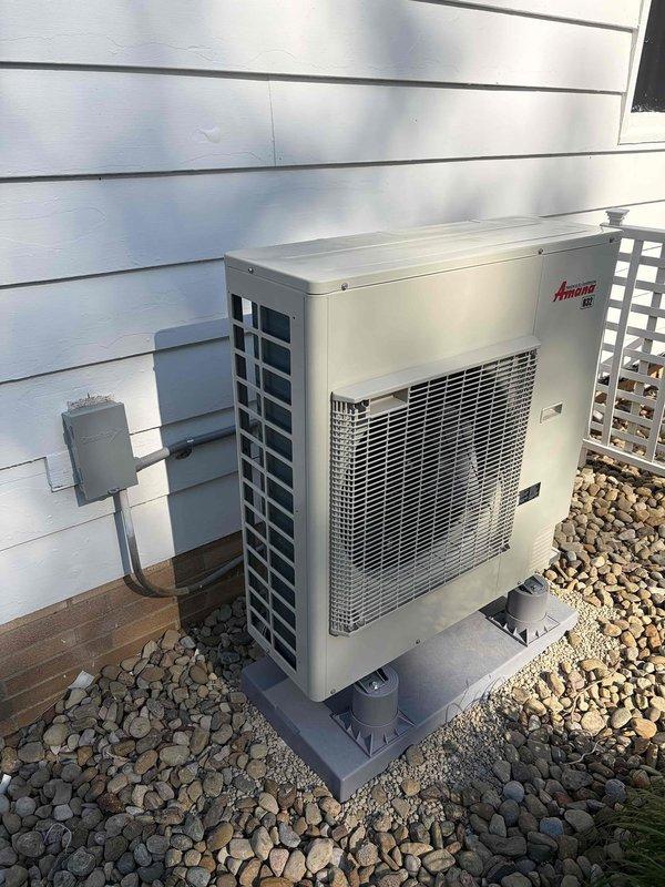 Completed installation of new Amana air conditioning condenser unit on exterior of residence. Unit was professionally mounted on plastic pad with decorative river rock base, electrical disconnect box installed with proper conduit connections, and system tested with return air temperature verified at 68.5°F.