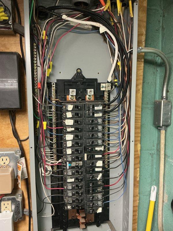 Completed electrical inspection of residential utility area, accessing property through rear entrance as requested. Documented electrical panel installation with dual-row circuit breaker configuration, verified proper wire management and secured connections at main terminal block. Inspected utility room mechanical connections including gas shut-off valve, CSST flexible gas connector line, and copper piping installations mounted to cinder block wall. All photographed components showed standard residential utility configurations with appropriate safety installations.