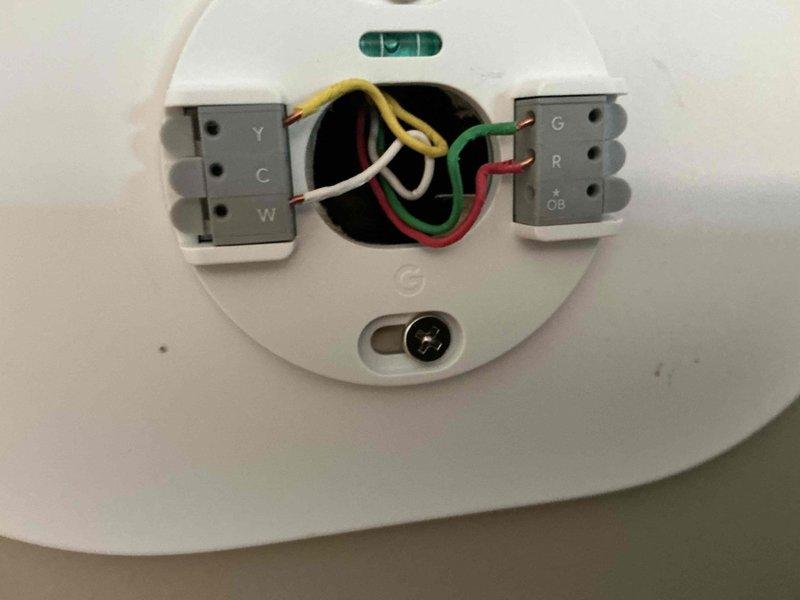 Conducted HVAC equipment assessment for system replacement at condo unit with easy accessibility. Evaluated existing thermostat wiring configuration with properly connected Y, C, W, G, R, and OB terminals, and inspected outdoor condenser unit positioned on concrete pad with decorative rock surround against brick wall exterior. Documented current equipment conditions and provided replacement options for complete system upgrade.
