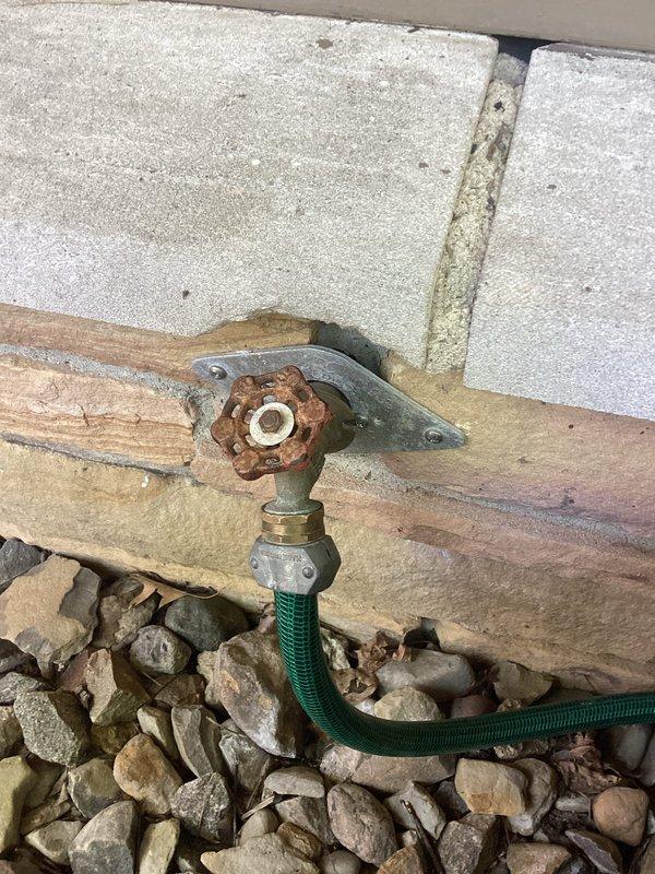 Replaced deteriorated outdoor water spigot featuring severely rusted valve handle and compromised fittings. The existing hose bib showed extensive oxidation and weathering, with water staining evident on surrounding siding, indicating potential leakage issues. Removed old galvanized pipe assembly, installed new frost-free sillcock with proper sealing to prevent future water intrusion and damage to building exterior.