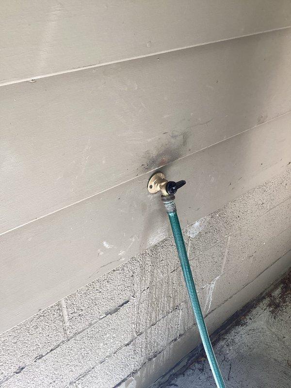 Replaced deteriorated outdoor water spigot featuring severely rusted valve handle and compromised fittings. The existing hose bib showed extensive oxidation and weathering, with water staining evident on surrounding siding, indicating potential leakage issues. Removed old galvanized pipe assembly, installed new frost-free sillcock with proper sealing to prevent future water intrusion and damage to building exterior.