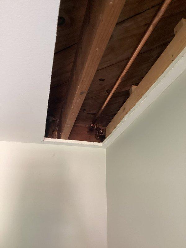 Returned to complete piping repair in exposed ceiling area with copper and PVC lines running along structural beams. Successfully finished installation of pipe joints, fittings, and valve connections, ensuring proper routing and secure mounting to ceiling joists.