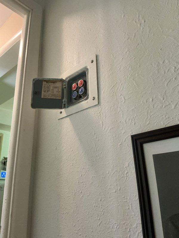 Completed mid-morning electrical inspection of residential property. Documented water meter installation in utility access area, including Neptune brand meter with copper and brass fittings connected to PVC piping, and photographed wall-mounted electrical control panel with multi-button interface in interior hallway for service records.