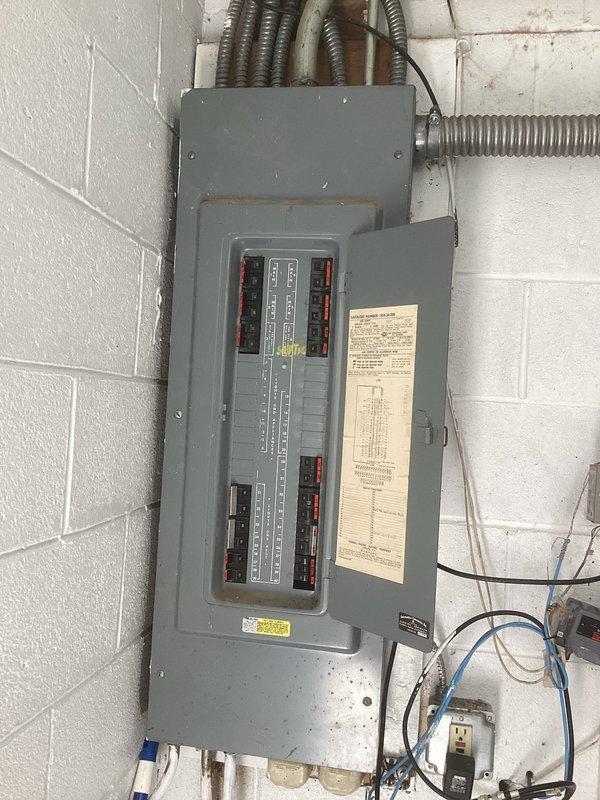 Conducted comprehensive electrical estimate for generator replacement at residential property. Customer's existing 20-year-old generator requires removal and replacement with new unit. Performed detailed load calculations per 2023 NEC Article 220 to properly size replacement generator, including general lighting load (15,600 VA floor area), small appliance and laundry branch circuits, electric clothes dryer (5.0 kW), cooking ranges (13.5 kW nameplate), HVAC loads (3-ton unit), fixed electric space heating, and various appliance loads including central vacuum, electric vehicle charger, spa/hot tub, tankless water heater, and wine cooler. Calculated motor loads for sump pump, garbage disposal, and elevator per NEC 220.50 and 220.14. Documented existing electrical panel installation showing aged breaker panel with multiple circuit breakers, flexible metal conduit entries, and associated wiring infrastructure mounted on interior block wall. Load calculation spreadsheet completed to determi