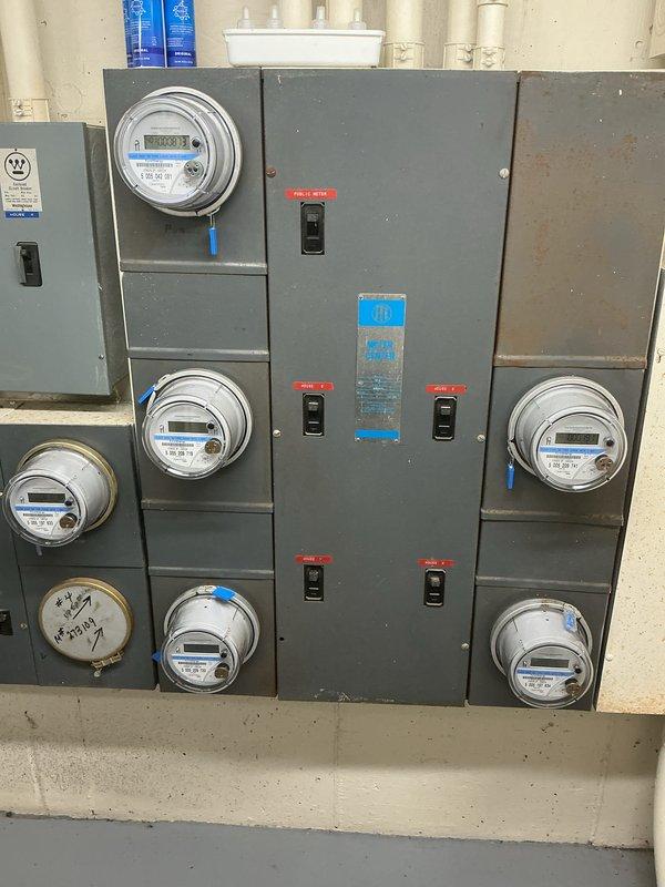 Conducted comprehensive electrical inspection of property focusing on exterior and interior electrical systems. Inspected exterior GFCI outlet mounted beneath building structure, verifying proper weatherproof enclosure installation and ground fault protection functionality. Evaluated multi-unit meter bank installation in utility area, documenting configuration of circuit breaker panel and multiple digital smart meters serving separate circuits. Photographed all inspected components for record-keeping purposes.