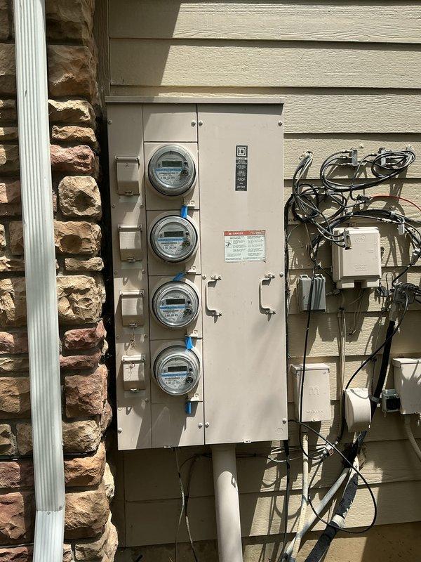 Conducted comprehensive electrical inspection of multi-unit dwelling service installation. Documented exterior meter bank configuration consisting of four digital meters with protective enclosures, associated disconnect switches, conduit runs, and junction boxes mounted on building exterior. Photographed interior electrical components and copper piping system for compliance verification and record-keeping purposes.