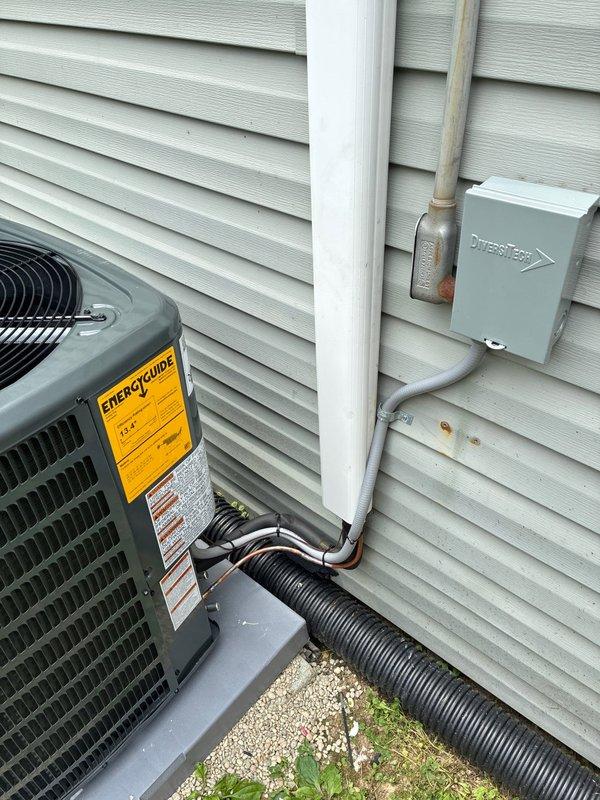 Completed full HVAC system replacement to resolve no cooling condition. Installed new Goodman brand air conditioning condensing unit on concrete pad with proper clearances from building structure. Unit positioned against light green vinyl siding with adequate airflow access on all sides. Connected refrigerant lines with proper insulation wrapping, secured copper line sets along foundation. Installed 80% efficiency furnace as part of complete system upgrade.

Electrical work included mounting disconnect box and conduit to exterior wall, ensuring proper power supply to outdoor unit. Installed white PVC piping for condensate drainage with proper termination and capping. All refrigerant line sets properly insulated and secured to building exterior. Wiring connections completed per manufacturer specifications with appropriate gauge wire and conduit protection.

System positioned on level concrete pad over prepared gravel base for drainage and stability. All penetrations through building env