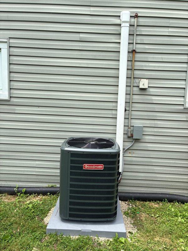 Completed full HVAC system replacement to resolve no cooling condition. Installed new Goodman brand air conditioning condensing unit on concrete pad with proper clearances from building structure. Unit positioned against light green vinyl siding with adequate airflow access on all sides. Connected refrigerant lines with proper insulation wrapping, secured copper line sets along foundation. Installed 80% efficiency furnace as part of complete system upgrade.

Electrical work included mounting disconnect box and conduit to exterior wall, ensuring proper power supply to outdoor unit. Installed white PVC piping for condensate drainage with proper termination and capping. All refrigerant line sets properly insulated and secured to building exterior. Wiring connections completed per manufacturer specifications with appropriate gauge wire and conduit protection.

System positioned on level concrete pad over prepared gravel base for drainage and stability. All penetrations through building env