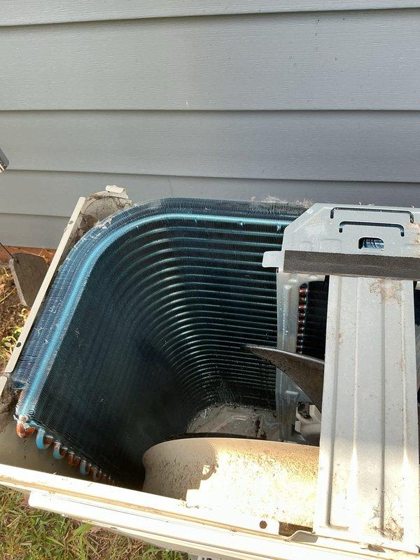 Responded to return service call for mini split system with no cooling condition where outdoor condenser unit was intermittently shutting down. Upon inspection, found outdoor unit's condenser coil heavily contaminated with dirt and debris buildup between fins, significantly restricting airflow and causing unit to overheat and cycle off on safety controls. Coil also showed evidence of corrosion along edges and rust staining on cabinet panels, indicating extended exposure to environmental elements without proper maintenance. Removed top cover to access internal components and documented condition of condenser coil assembly and fan section, noting accumulated dust and oxidation on metal surfaces throughout unit. Heavy debris accumulation between coil fins was identified as primary cause of reduced heat transfer efficiency, leading to high head pressure and thermal shutdown of compressor.