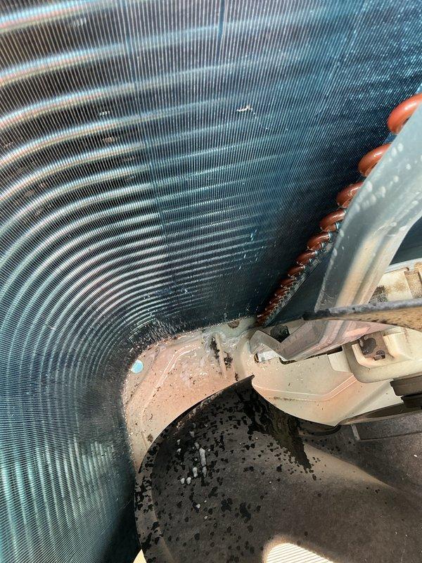 Responded to return service call for mini split system with no cooling condition where outdoor condenser unit was intermittently shutting down. Upon inspection, found outdoor unit's condenser coil heavily contaminated with dirt and debris buildup between fins, significantly restricting airflow and causing unit to overheat and cycle off on safety controls. Coil also showed evidence of corrosion along edges and rust staining on cabinet panels, indicating extended exposure to environmental elements without proper maintenance. Removed top cover to access internal components and documented condition of condenser coil assembly and fan section, noting accumulated dust and oxidation on metal surfaces throughout unit. Heavy debris accumulation between coil fins was identified as primary cause of reduced heat transfer efficiency, leading to high head pressure and thermal shutdown of compressor.