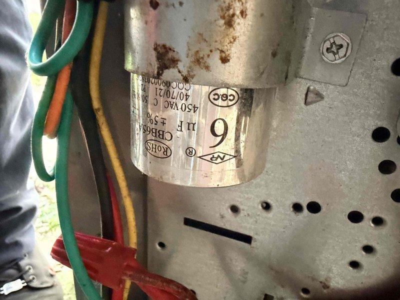 Responded to emergency no-cool call on a 6-year-old central air conditioning system where the condenser fan was not operating. Upon arrival, inspected the outdoor condensing unit and identified a failed dual run capacitor exhibiting visible corrosion and rust deterioration on the cylindrical housing. The capacitor showed significant environmental wear consistent with outdoor exposure. Verified electrical connections and wiring integrity at the component. Replaced the defective capacitor with manufacturer-specified replacement unit rated at 407/21V, 250VAC. Tested system operation and confirmed condenser fan motor startup and proper rotation. Verified cooling cycle initiation and normal compressor operation. System restored to full cooling functionality.