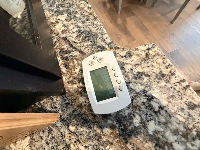 Responded to no cooling call at residential property. Upon arrival, found thermostat displaying but system not responding to cooling commands. Removed thermostat from wall plate to inspect wiring connections and verify proper 24V power supply. All wiring connections were secure and voltage readings confirmed adequate power to thermostat. Determined thermostat had failed and was not sending call signal to outdoor condensing unit. Discussed replacement options with homeowner and temporarily removed faulty thermostat for customer review of upgrade options before reinstallation of new unit.
