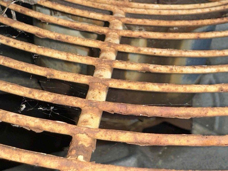 Responded to no cooling call on 15+ year old central air conditioning system. Upon arrival, conducted visual inspection of outdoor condensing unit. Found unit located in overgrown area with significant vegetation encroachment, including ferns and ground cover growing around equipment base. Observed severely corroded condenser coil with extensive rust buildup on metal fins and grating, indicating prolonged exposure to moisture and lack of maintenance. Coil deterioration was advanced enough to compromise heat transfer efficiency and airflow. Noted drainage components and refrigerant lines partially obscured by mulch, leaves, and plant debris. Given the age of equipment, extent of corrosion damage, and reduced system capacity, recommended replacement of outdoor unit rather than repair. Discussed options with customer for new high-efficiency system installation.