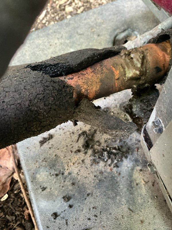 Responded to no cooling complaint for residential air conditioning system. Upon arrival, inspected outdoor unit and discovered severely corroded copper refrigerant line penetrating through foundation wall. Line showed extensive oxidation with green patina and orange-brown deterioration, indicating prolonged exposure to moisture and potential refrigerant leak. Documented condition of corroded piping and valve connections showing weathering and mineral deposits. System unable to maintain proper cooling due to compromised refrigerant lines requiring replacement and proper sealing at foundation penetration point.