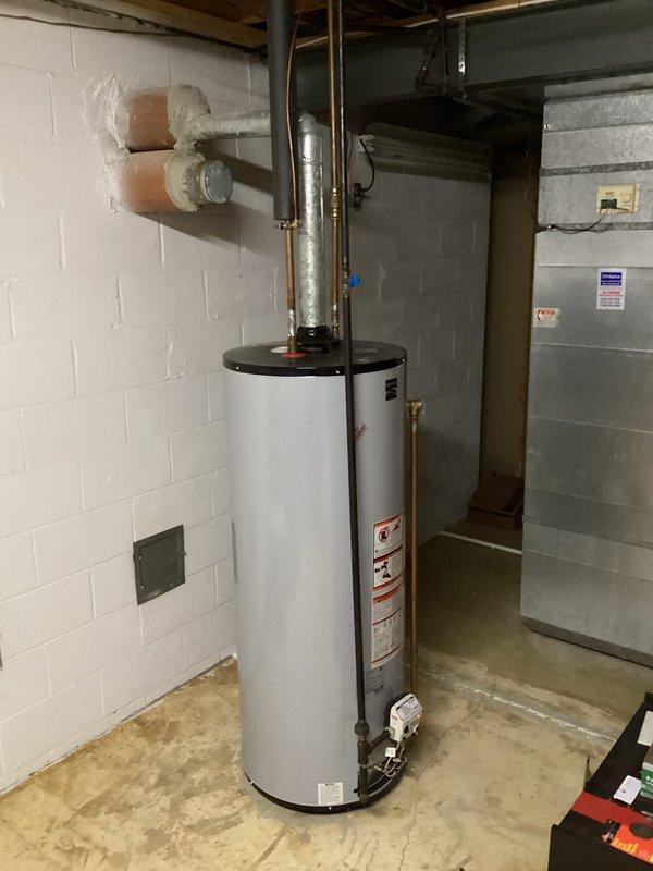 Responded to service call for tanked water heater producing lukewarm water. Performed diagnostic inspection of residential water heater unit located in basement mechanical room. Assessed unit specifications, examined inlet and outlet connections, and verified proper venting configuration through metallic exhaust pipe. Inspected surrounding plumbing infrastructure including copper supply lines and associated HVAC systems in utility area. Documented equipment condition and installation setup with photographic records showing water heater placement, wall-mounted utilities, and basement infrastructure. Provided assessment findings and recommendations to household representatives present during service visit.