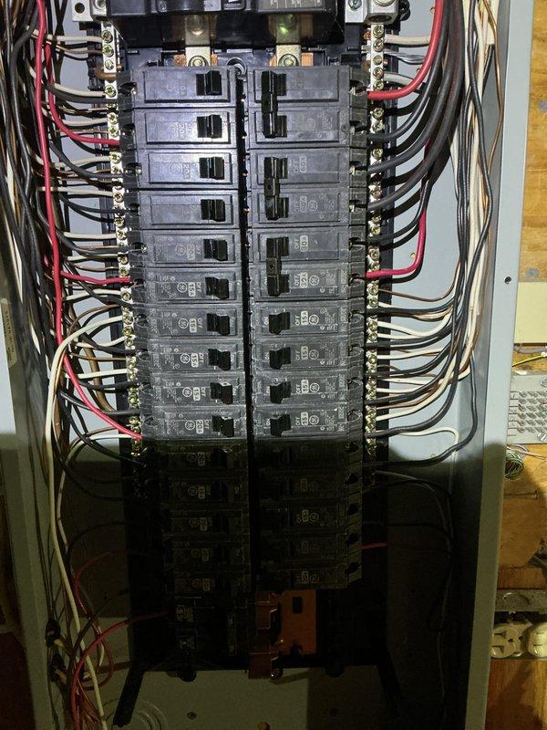 Conducted mid-morning electrical inspection of residential service panel and utility systems. Documented existing electrical panel configuration showing dual-column breaker arrangement with approximately 20-24 circuit breakers, verified proper wire management and connections to bus bars, and confirmed organized installation of branch circuits. Also photographed adjacent plumbing assembly with water meter/pressure regulator and shutoff valve for reference during inspection.