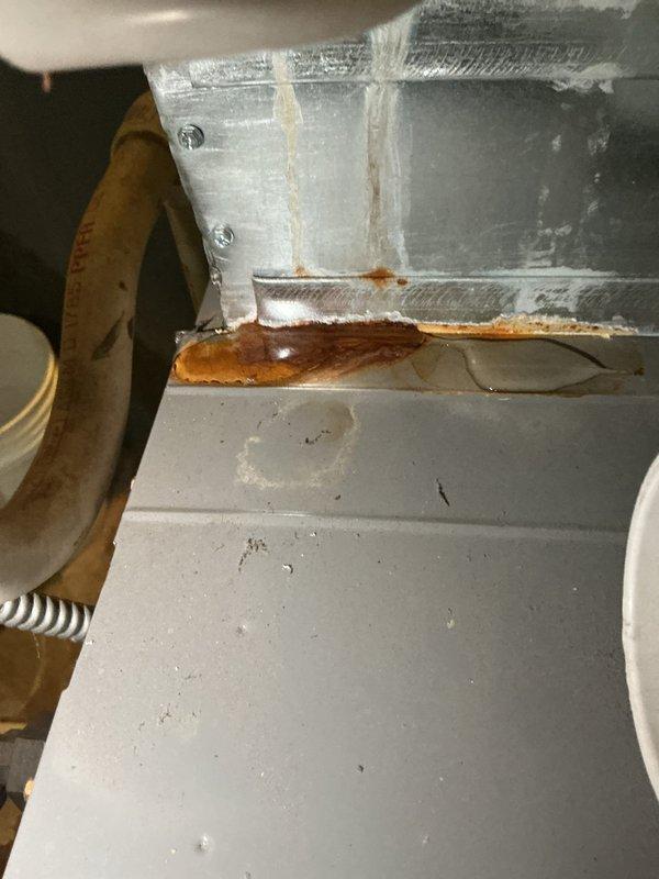 Responded to A/C unit leaking from pipes. Upon inspection, identified active water leak originating from refrigerant line connections with visible rust corrosion and moisture damage on evaporator housing and condensate components. Documented existing conditions showing rust streaking on metal surfaces and water staining around pipe joints, indicating ongoing leak issue requiring repair of compromised piping connections.