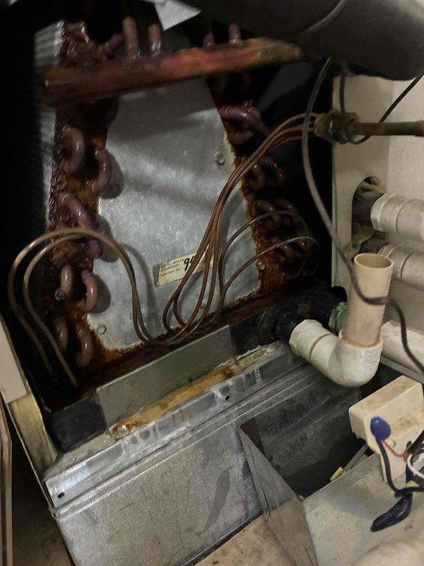 Responded to call for air conditioning system leaking from supply vent. Upon inspection, discovered severely corroded evaporator coil and condensate drain system with extensive rust buildup on copper refrigerant lines and connections. The condensate drain pan showed significant deterioration with mineral deposits and corrosion staining, indicating long-term moisture issues and inadequate drainage. Documented existing conditions showing the compromised state of HVAC components including heat exchanger assembly and drainage piping requiring immediate attention to prevent further water damage and system failure.
