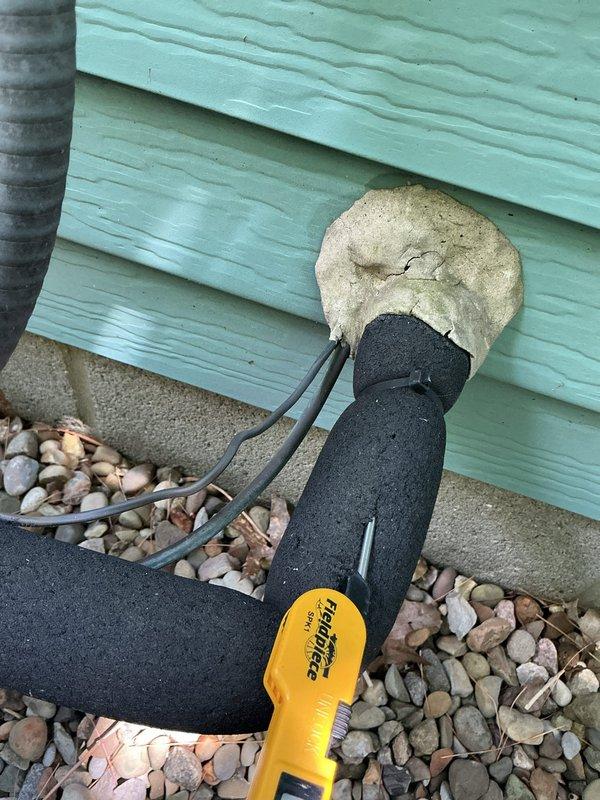 Responded to no cooling complaint on residential AC system installed in May 2023. Upon arrival, discovered refrigerant line insulation had deteriorated significantly, with foam sleeve showing severe weathering and breakdown at the foundation penetration point. The compromised insulation was allowing heat transfer to the suction line, reducing system efficiency and cooling capacity. Assessed the line set penetration through the building exterior, noting inadequate sealing at the entry point. Documented the condition of the deteriorated insulation sleeve and penetration seal for replacement recommendation. System requires new line set insulation and proper sealing of the wall penetration to restore full cooling performance and prevent further efficiency loss.