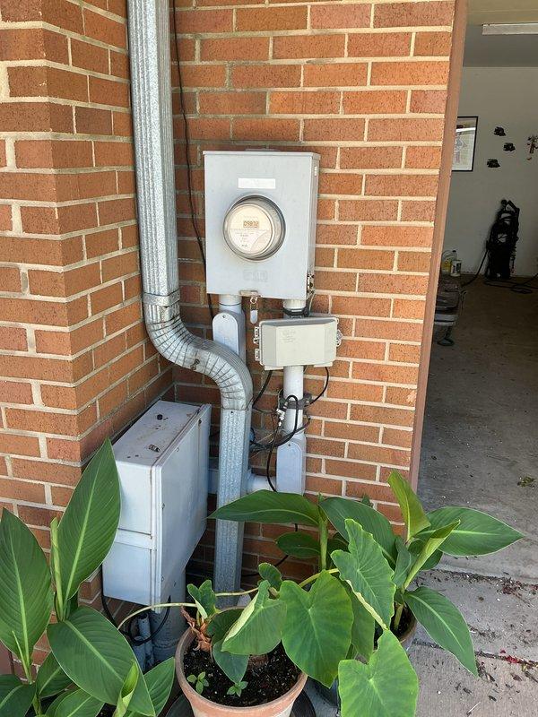 Completed electrical inspection of residential service entrance and main distribution panel. Documented exterior meter installation, service conduit routing, and associated utility connections mounted on brick exterior wall. Verified proper installation of flexible conduit connecting to ground-level equipment. Inspected interior main electrical panel containing split-bus configuration with dual main breaker assemblies and approximately 20-24 branch circuit breakers. Confirmed proper wire routing, conductor organization, and grounding connections throughout panel. All circuit breakers, wire terminations, and electrical connections photographed for record.