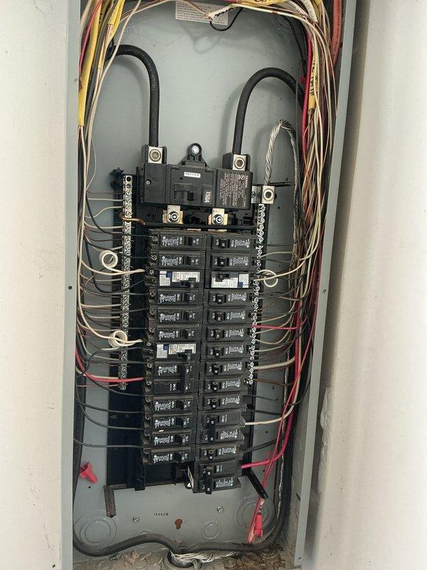 Completed electrical inspection of residential service entrance and main distribution panel. Documented exterior meter installation, service conduit routing, and associated utility connections mounted on brick exterior wall. Verified proper installation of flexible conduit connecting to ground-level equipment. Inspected interior main electrical panel containing split-bus configuration with dual main breaker assemblies and approximately 20-24 branch circuit breakers. Confirmed proper wire routing, conductor organization, and grounding connections throughout panel. All circuit breakers, wire terminations, and electrical connections photographed for record.