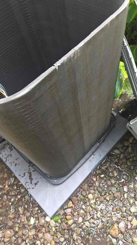 Arrived on site for scheduled chemical coil wash service on outdoor condensing unit. Customer confirmed prior payment arrangement for this cleaning service. Documented pre-service condition of unit showing heavy accumulation of dirt, dust, and debris throughout exterior coil fins with grayish-brown discoloration, particularly concentrated on lower sections. Unit positioned on concrete pad with plastic drain pan, surrounded by landscaping vegetation. Photographic documentation captured the extent of coil contamination and overall unit condition prior to scheduled chemical cleaning treatment.