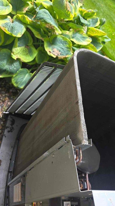 Arrived on site for scheduled chemical coil wash service on outdoor condensing unit. Customer confirmed prior payment arrangement for this cleaning service. Documented pre-service condition of unit showing heavy accumulation of dirt, dust, and debris throughout exterior coil fins with grayish-brown discoloration, particularly concentrated on lower sections. Unit positioned on concrete pad with plastic drain pan, surrounded by landscaping vegetation. Photographic documentation captured the extent of coil contamination and overall unit condition prior to scheduled chemical cleaning treatment.